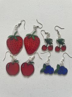 six strawberrys and blueberries are hanging from silver earwires on a white surface