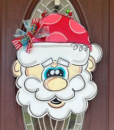 a door hanger with a santa clause on it's face and candy canes in his mouth