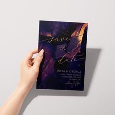 a hand holding up a purple and gold save the date card