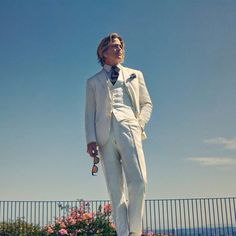 a man in a white suit and sunglasses standing on top of a rock with flowers behind him