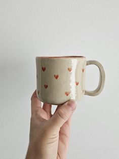 a hand holding a coffee cup with hearts painted on the outside and inside, in front of a white wall