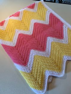 a crocheted dishcloth is sitting on a white counter top with yellow, red and pink colors