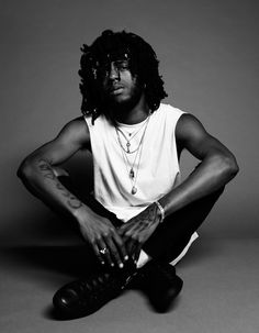 a black and white photo of a man with dreadlocks sitting on the floor