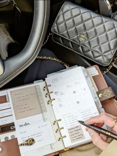 a person holding a pen and writing in a planner book next to a handbag