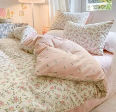 an unmade bed with pink and blue floral bedspread, pillows and blankets