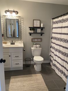 a white toilet sitting under a bathroom mirror next to a sink and a shower curtain