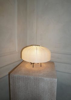 a table lamp sitting on top of a block of concrete in a room with white walls