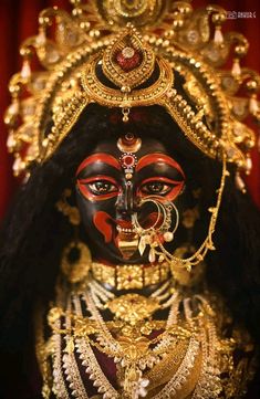 an elaborately decorated mask is displayed in front of a red curtain