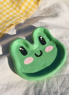 a green bowl with a face painted on it sitting on top of a white blanket