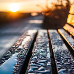 a close up of a bench with the sun setting in the back ground behind it