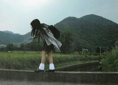 a woman with long hair is standing on the side of a road in front of mountains