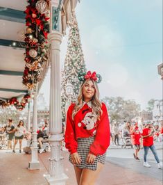 a woman standing in front of a christmas tree wearing a mickey mouse sweater and skirt