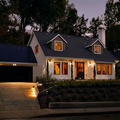 a house lit up at night with lights on the front and garage door, driveway leading to it