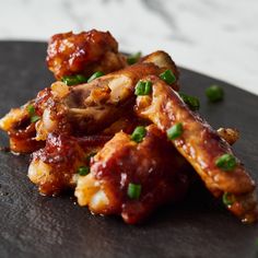 chicken wings with sauce and green onions on a black plate