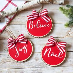 three ornaments with red and white ribbons on them sitting on a wooden table next to some branches