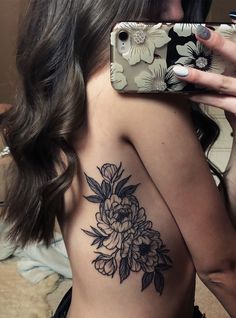 a woman taking a selfie with her cell phone and flower tattoo on her back