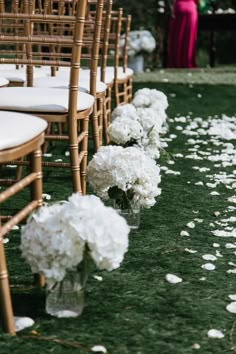 rows of chairs lined up with white flowers on the grass and petals down the aisle