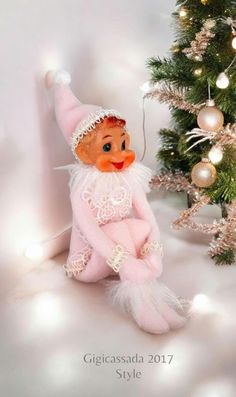 a small doll sitting next to a christmas tree