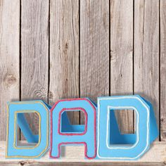 the word dad spelled with colored letters on a wooden surface next to a wood fence