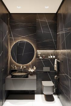 a modern bathroom with black marble walls and flooring, along with a round mirror on the wall