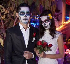 a man and woman dressed up as skeleton bride and groom for halloween wedding ceremony with flowers in their hands