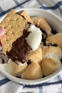 a person holding up a piece of food in a bowl filled with marshmallows and chocolate