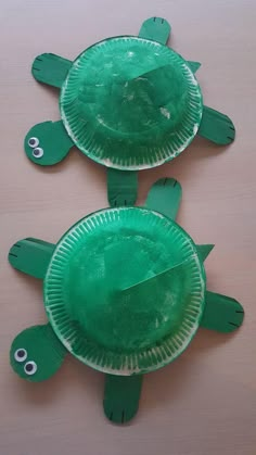 two paper plates shaped like turtles sitting on top of a wooden table next to each other