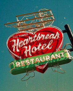 a heart shaped sign hanging from the side of a building next to a neon sign