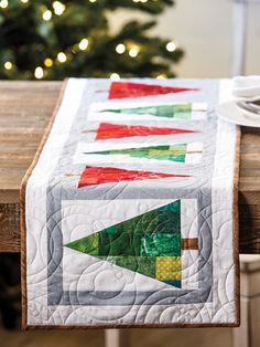 a quilted table runner on a wooden table with a christmas tree in the background