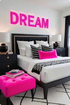 a white bed with pink pillows and black headboard next to a neon sign that reads dream