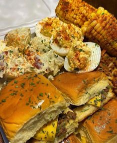 a white plate topped with sandwiches and corn on the cob next to other foods