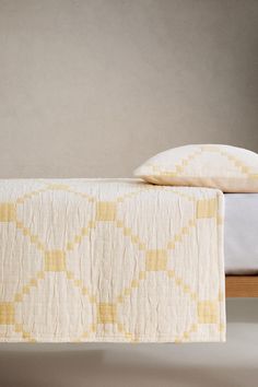 a bed with a white and yellow bedspread next to a wooden headboard