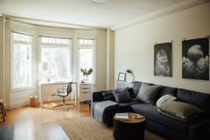 a living room filled with furniture next to two large windows and a wooden floor covered in hard wood floors