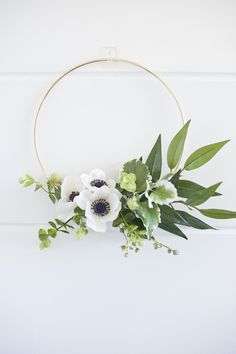 white flowers and greenery are arranged on a gold hoop hanging from the side of a wall