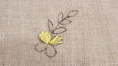 a small yellow flower sitting on top of a piece of linen covered in embroidery thread