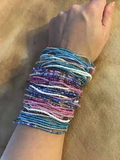 a woman's arm with several different colored bracelets on top of her hand