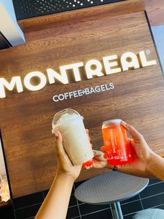 two people holding up drinks in front of a sign that reads montreaal coffee bagels