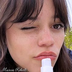 a close up of a person with a lip balm in her mouth and trees in the background