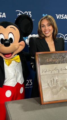 a woman standing next to mickey mouse at a press conference with a signed handprint