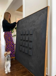 a woman standing next to a blackboard with letters on it and a dog looking at it