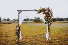 an outdoor wedding setup with white draping and flowers on the arch, in front of a grassy field