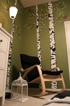 a bedroom decorated in green and white with birch trees on the wall, birdcage next to chair