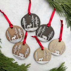 four christmas ornaments hanging from a tree branch with red ribbons on them and some deer in the woods