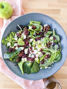 a salad with apples and cranberries in a blue bowl on a wooden table