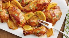 chicken wings with lemons and parsley on a white plate next to a fork