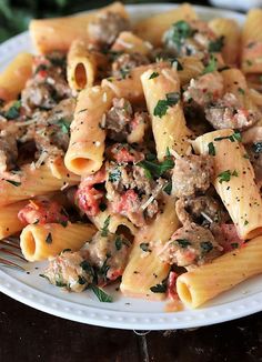 a white plate topped with pasta covered in meat and sauces on top of a wooden table