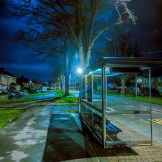 a bus stop sitting on the side of a road next to a street light at night