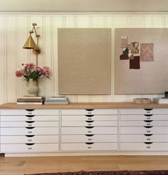 a white dresser with drawers and two pictures on the wall next to flowers in a vase