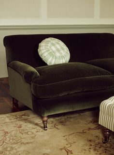 a green couch with a white pillow on it's back and an ottoman in the background