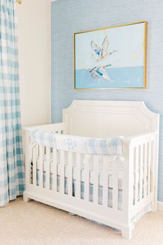 a white crib in a blue and white nursery with a painting on the wall